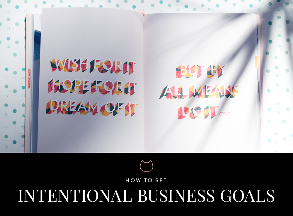 An open book has the words: "Wish for it. Hope for it. Dream it. But by all means do it." written in block letters of orange, yellow and red. It lies on a white and blue spotted backgorund. Across the bottom is a black bar with a small outline of a cat head in goals and the words How to set intentional business goals.
